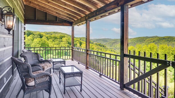 A covered porch with wicker furniture and a table, overlooking a forested landscape. - 95-acre Countryside Estate! Luxe Vermont Farmhouse (Chelsea)
