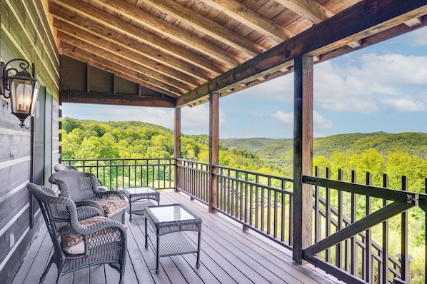 A covered porch with wicker furniture and a table, overlooking a forested landscape.