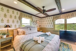 A bedroom with a bed, a ceiling fan, a dresser, and a window with a view.