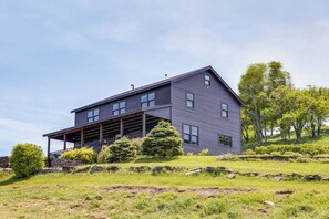 A two-story house with a covered porch, surrounded by a grassy landscape and trees. - 95-acre Countryside Estate! Luxe Vermont Farmhouse (Chelsea)