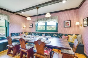 A dining area with a wooden table, chairs, and a bench. There are windows with curtains, wall-mounted lamps, and framed pictures. - 95-acre Countryside Estate! Luxe Vermont Farmhouse (Chelsea)