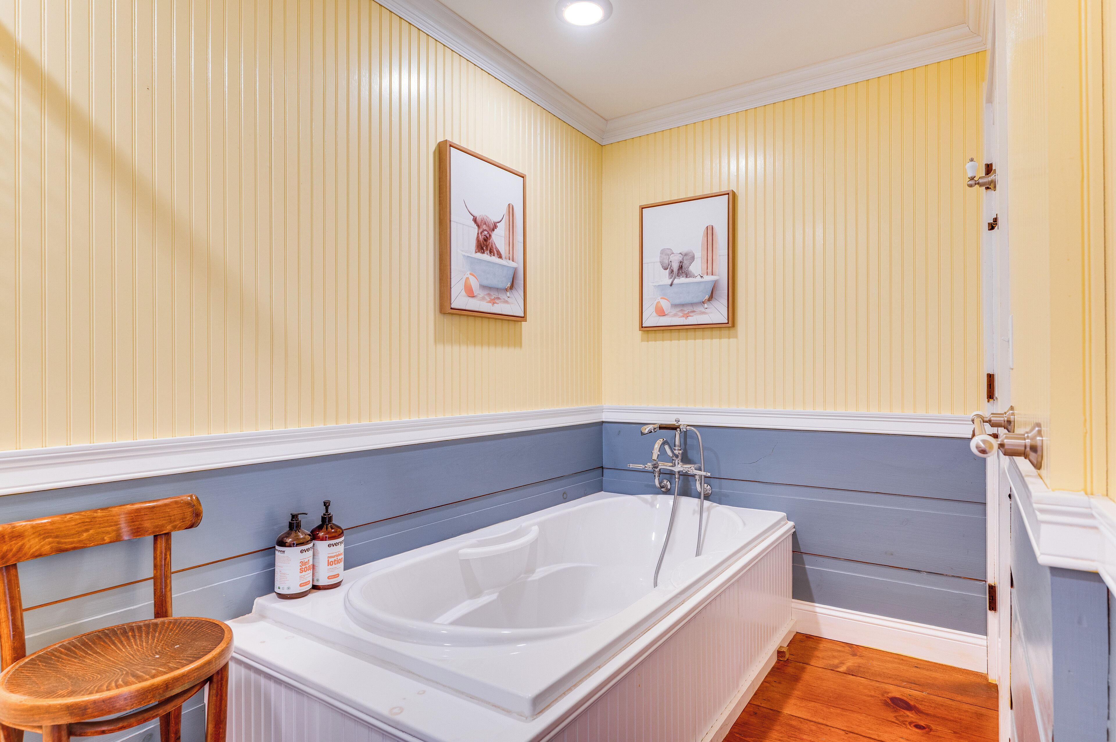 A bathroom with a bathtub, wooden chair, and two framed pictures on the wall.