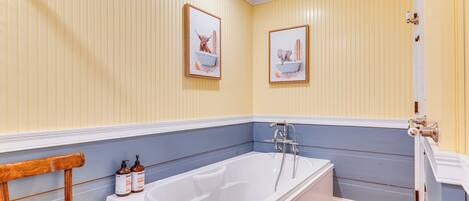 A bathroom with a bathtub, wooden chair, and two framed pictures on the wall.