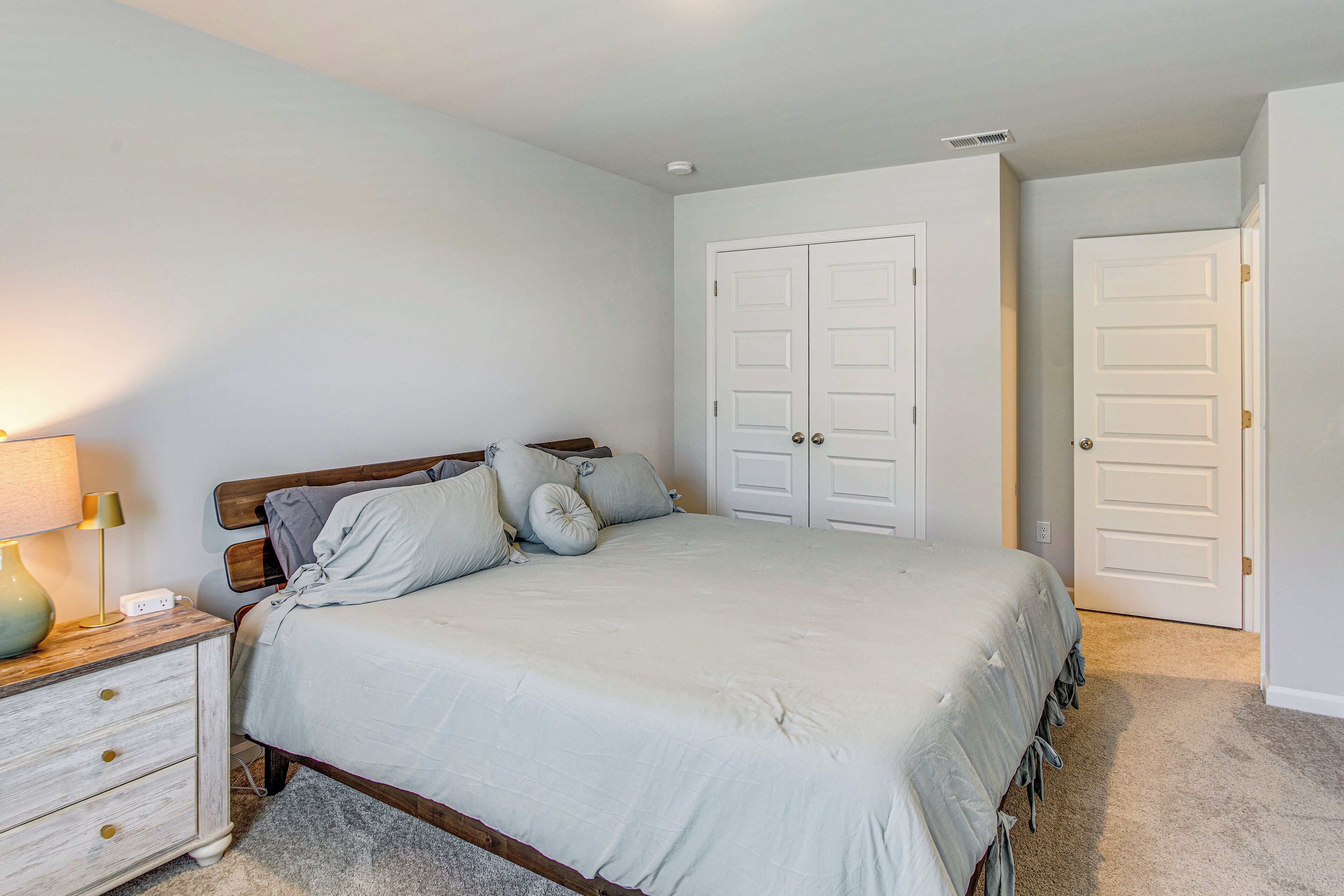 A bedroom with a bed, nightstand, lamp, and two white doors.