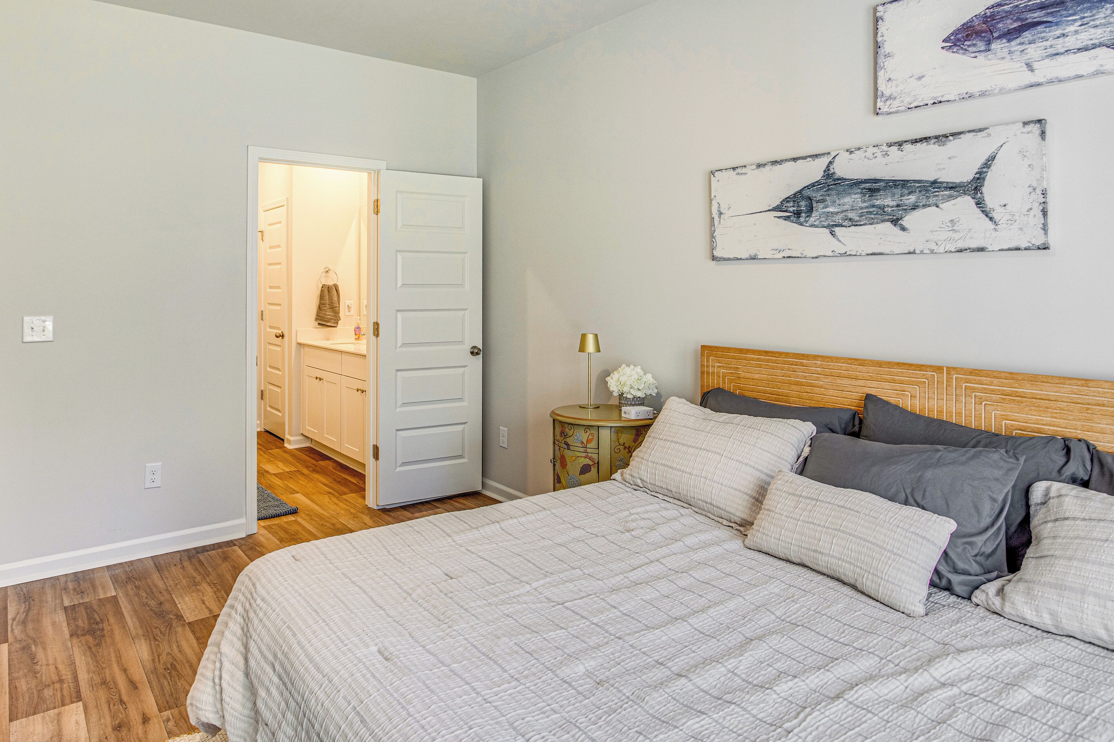 Une chambre à coucher comprenant un lit, une table de chevet, une lampe et deux tableaux représentant des poissons, accrochés au mur.