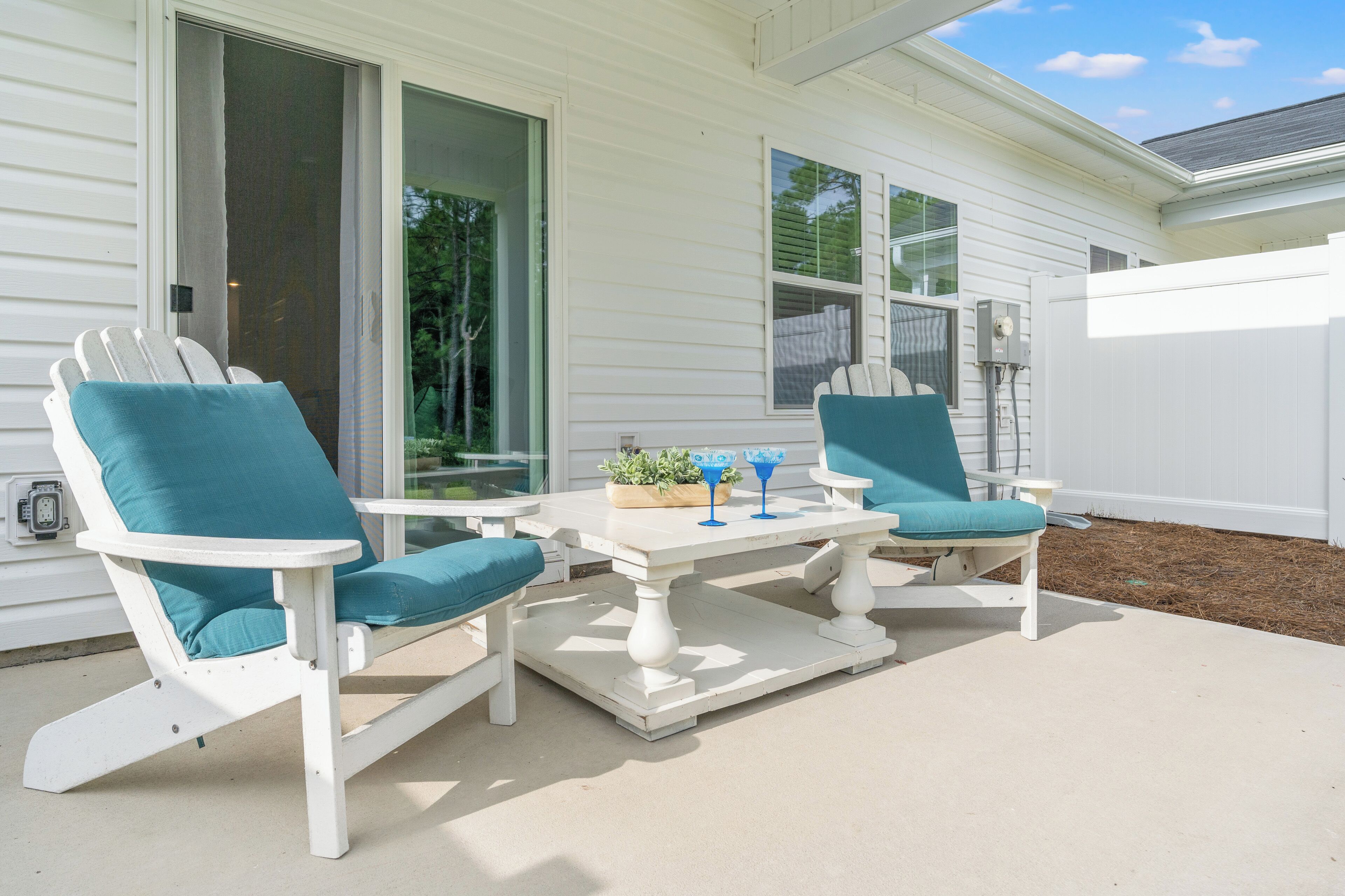 Une terrasse avec deux chaises Adirondack blanches et une table blanche, une porte-fenêtre coulissante et une clôture blanche.
