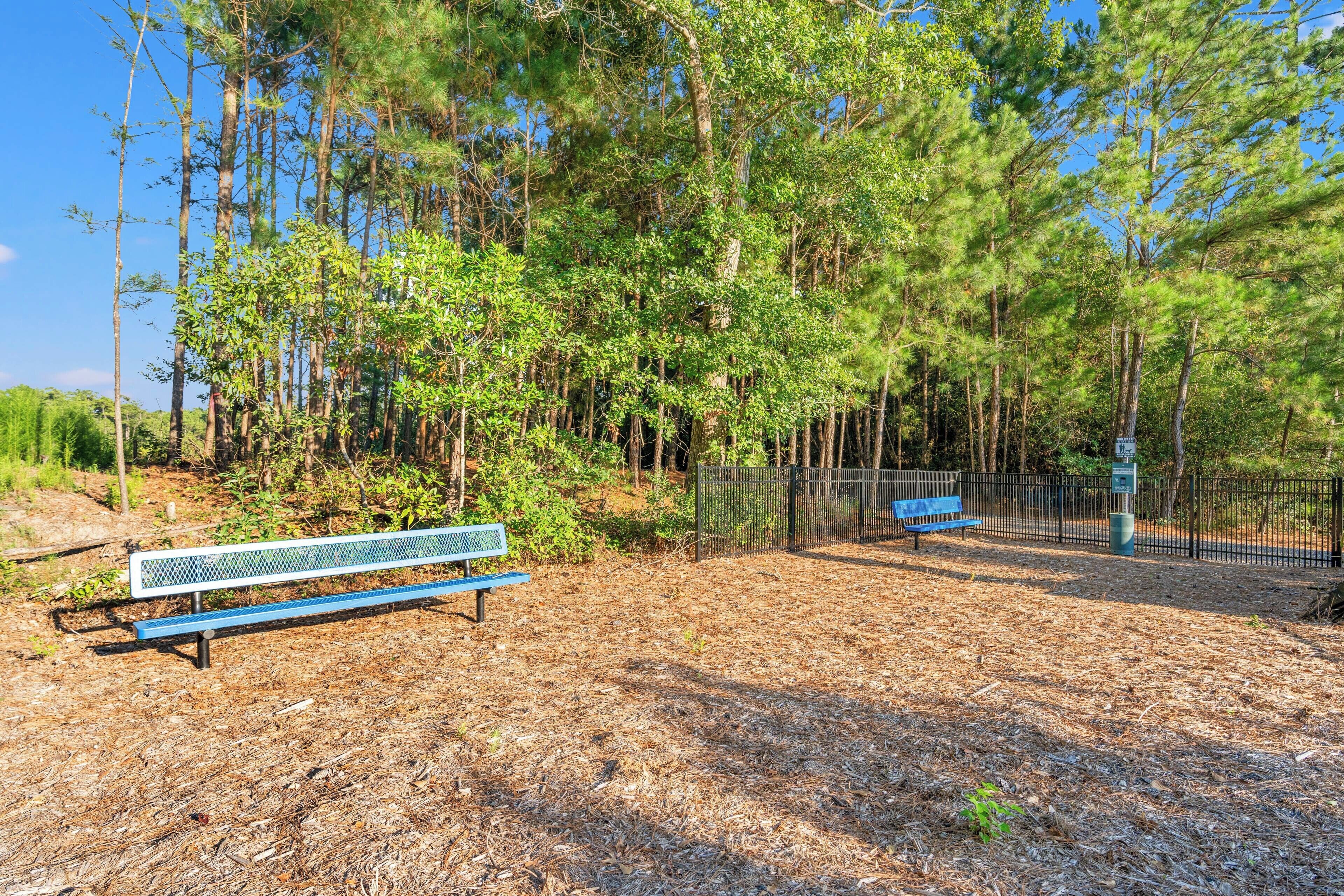 A park with two benches, a fence, and a wooded area.