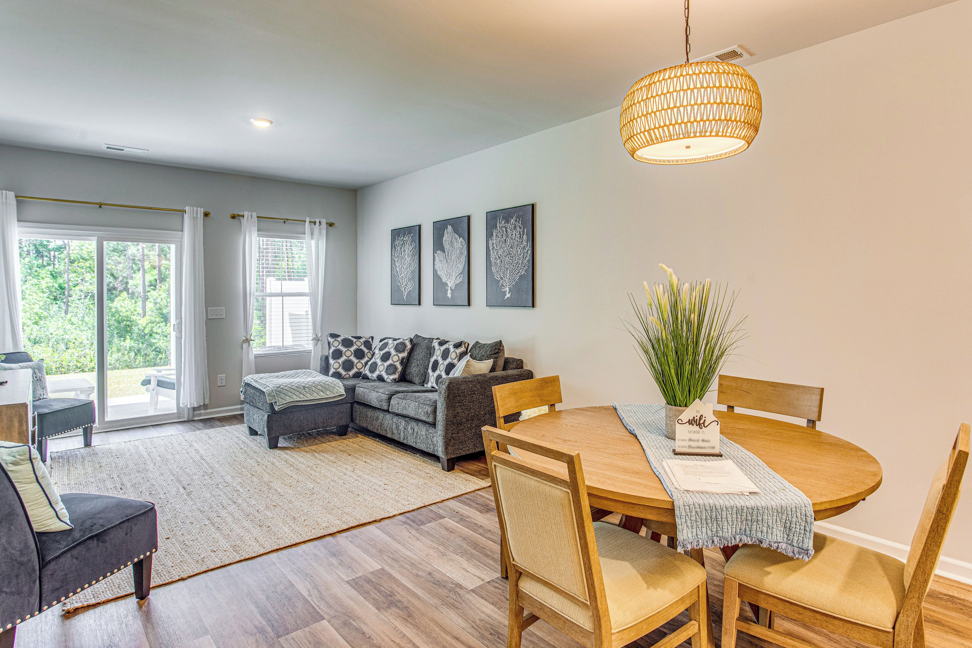 A modern living room with a sofa, dining table, and chairs, a large window, and a hanging light fixture.
