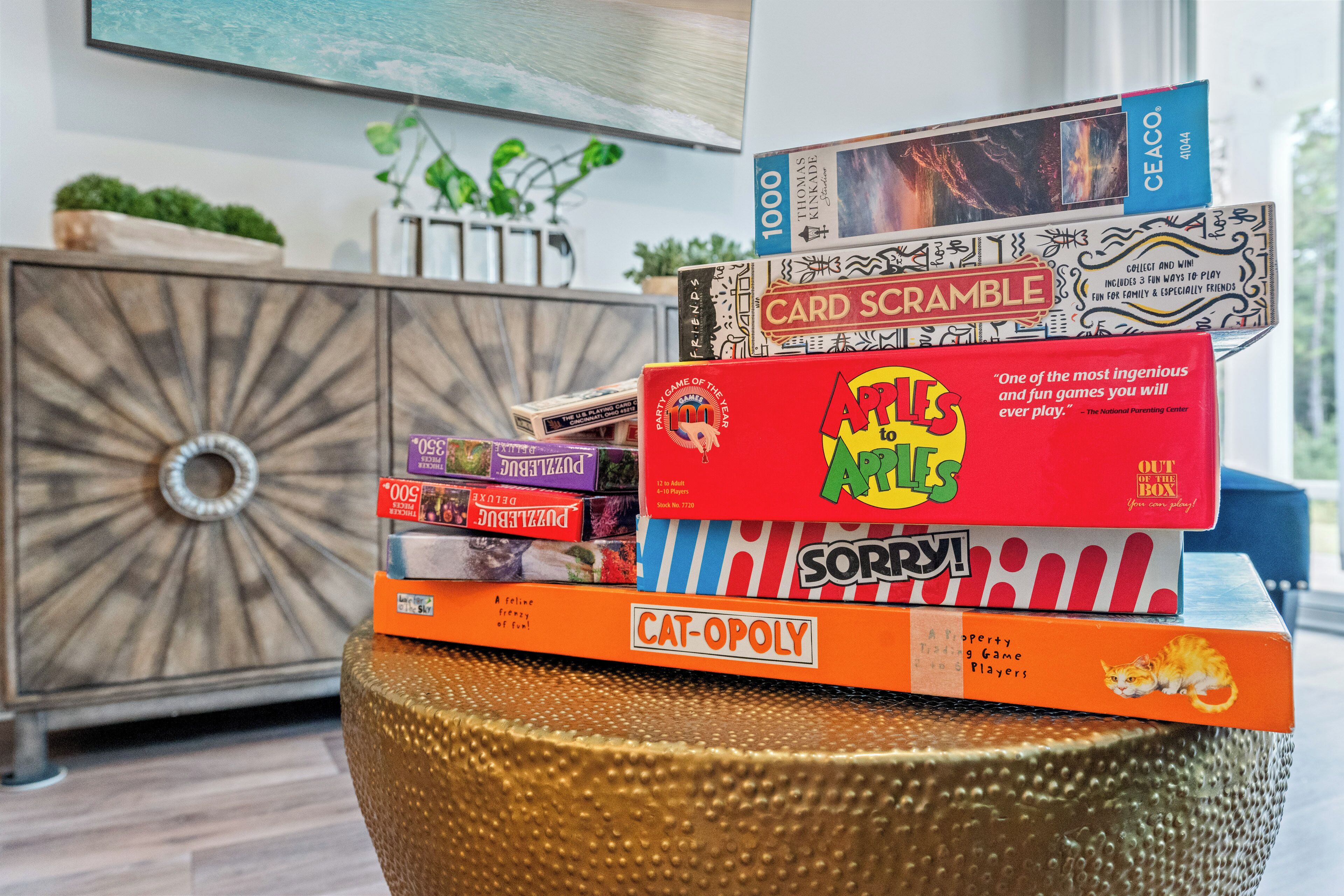 A stack of board games on a table with a decorative cabinet in the background.