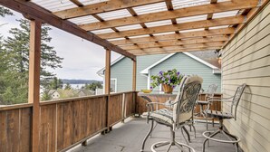 A covered outdoor patio with a wooden railing, metal chairs, a table, and a potted plant. - 3 Mi to Saint Paul Harbor! Scenic Group Retreat (Kodiak)