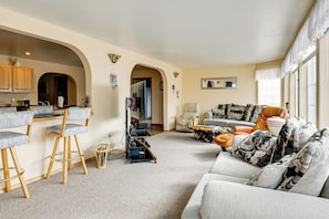 A living room with a sofa, a coffee table, and a bar area with stools. - 3 Mi to Saint Paul Harbor! Scenic Group Retreat (Kodiak)