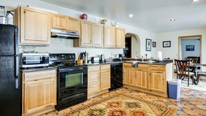 A kitchen with wooden cabinets, a microwave, stove, and a coffee maker. - 3 Mi to Saint Paul Harbor! Scenic Group Retreat (Kodiak)