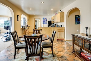A dining area with a round table and chairs, a kitchen with wooden cabinets, and a tiled floor. - 3 Mi to Saint Paul Harbor! Scenic Group Retreat (Kodiak)
