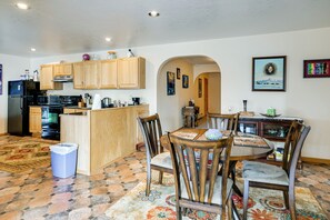 A kitchen with wooden cabinets, a dining area with a table and chairs, and a patterned rug on the floor.
