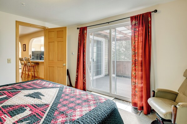A bedroom with a bed, a chair, a desk, and a sliding glass door to a balcony.