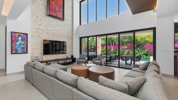 Ein modernes Wohnzimmer mit einem Ecksofa, einem Kamin und einem großen Fenster mit Blick auf einen Garten.