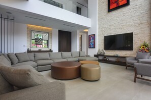 A modern living room with a sectional sofa, ottomans, a flat-screen TV, and artwork on the walls. - Steps to Sea! Luxury Cozumel Villa w/ Resort Perks (Cozumel)