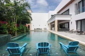 A modern pool area with three Adirondack chairs, a covered seating area, and a clear view of the pool. - Steps to Sea! Luxury Cozumel Villa w/ Resort Perks (Cozumel)