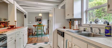 A kitchen with white cabinets, a dishwasher, a sink, and a window with a view of trees.