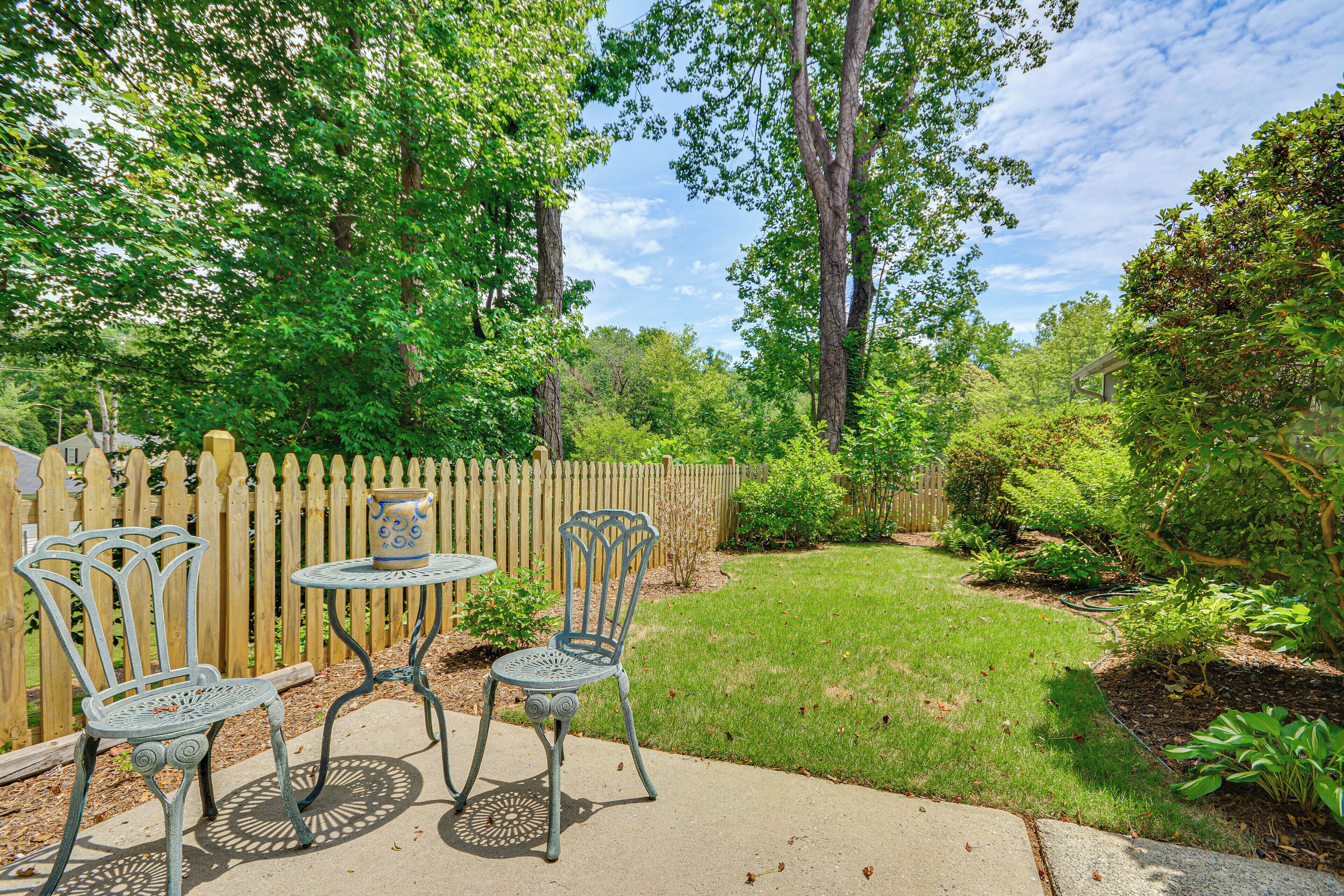 A patio with metal chairs and a table, surrounded by a wooden fence and lush greenery.