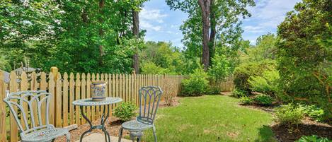 A patio with metal chairs and a table, surrounded by a wooden fence and lush greenery.