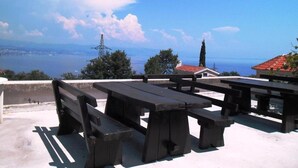 Outdoor picnic tables with a view of a body of water and distant cityscape. - Sea View Apt With Terrace Kitchen (Opatija)