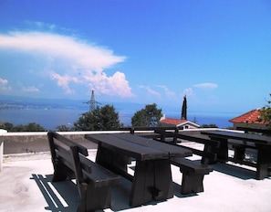 Outdoor picnic tables with a view of a body of water and distant cityscape. - Sea View Apt With Terrace Kitchen (Opatija)