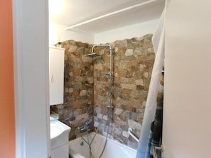 A bathroom with a stone wall, a shower, a sink, and a toilet. - Sea View Apt With Terrace Kitchen (Opatija)