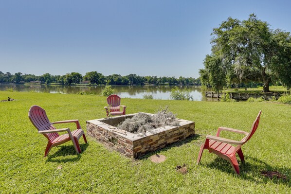 A lakeside view with a fire pit and Adirondack chairs.