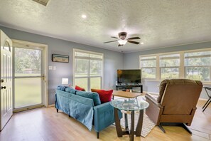 A living room with a blue sofa, a brown chair, a glass coffee table, a ceiling fan, and a TV.