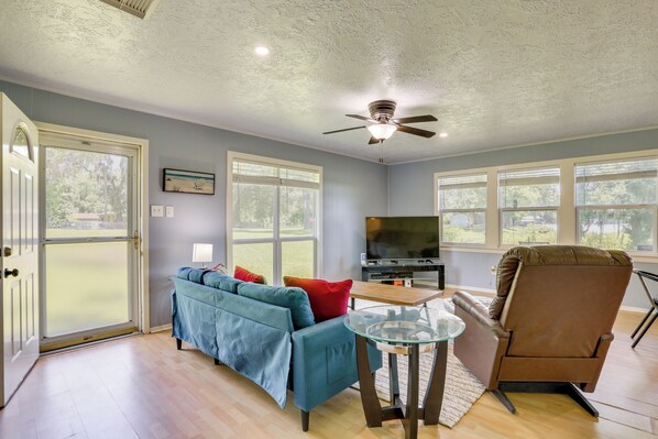 A living room with a blue sofa, a brown chair, a glass coffee table, a ceiling fan, and a TV.