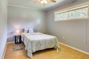 Une chambre à coucher avec un lit, une table de chevet, une lampe, une fenêtre et un ventilateur de plafond.