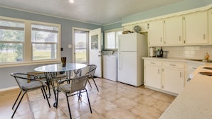 A kitchen with a dining table and chairs, a refrigerator, and a window with blinds.