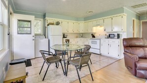 A compact kitchen with white cabinets, a glass dining table, wicker chairs, and a brown leather chair.