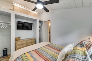 Ein Schlafzimmer mit einem Bett, einem an der Wand montierten Fernseher, einem Deckenventilator und einem Kleiderschrank.