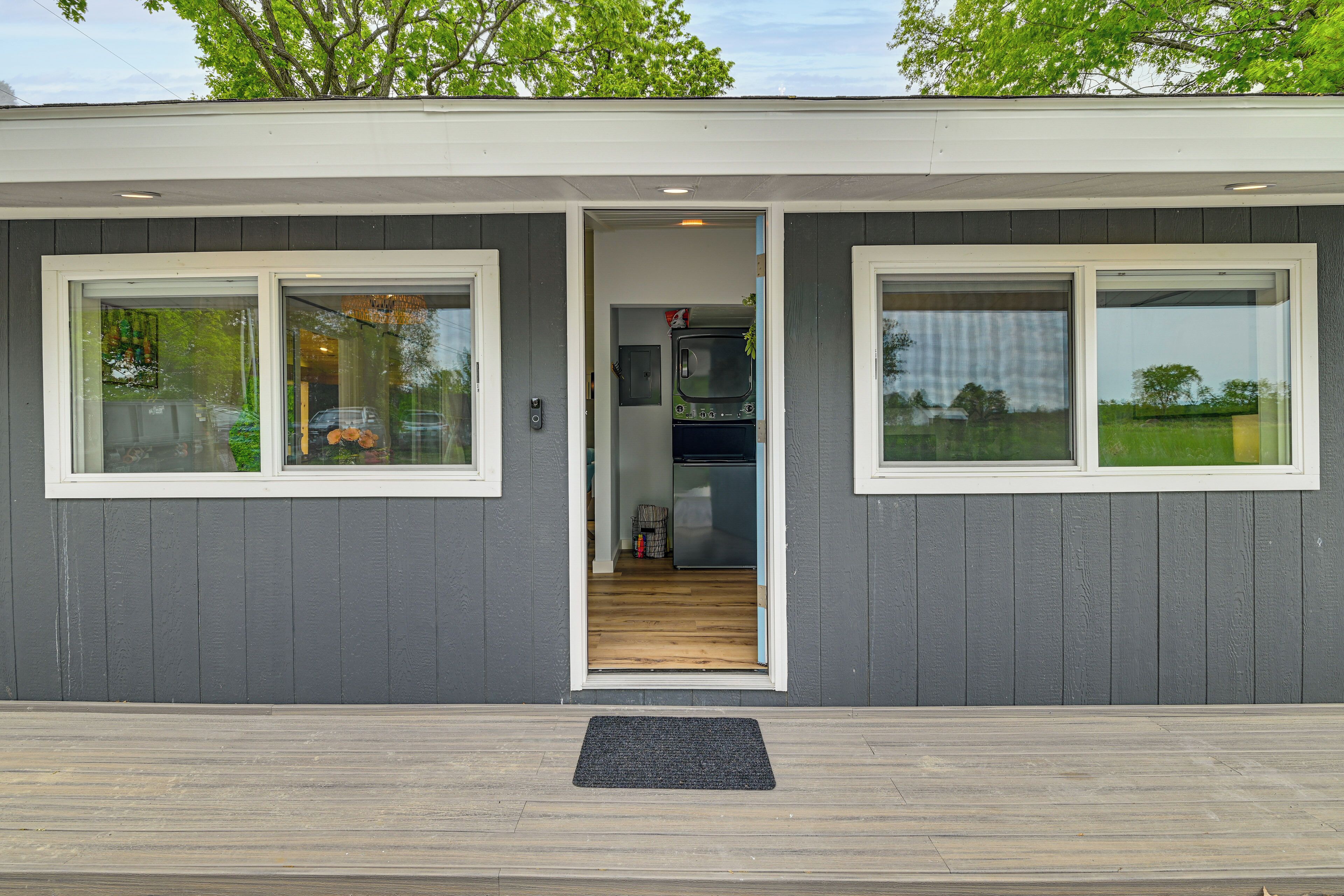 Un bâtiment moderne à l’extérieur gris, doté d’une terrasse en bois et d’une porte d’entrée donnant sur un espace intérieur comprenant un coin cuisine.