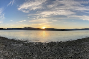 A calm lake at sunset with a clear sky and distant mountains.