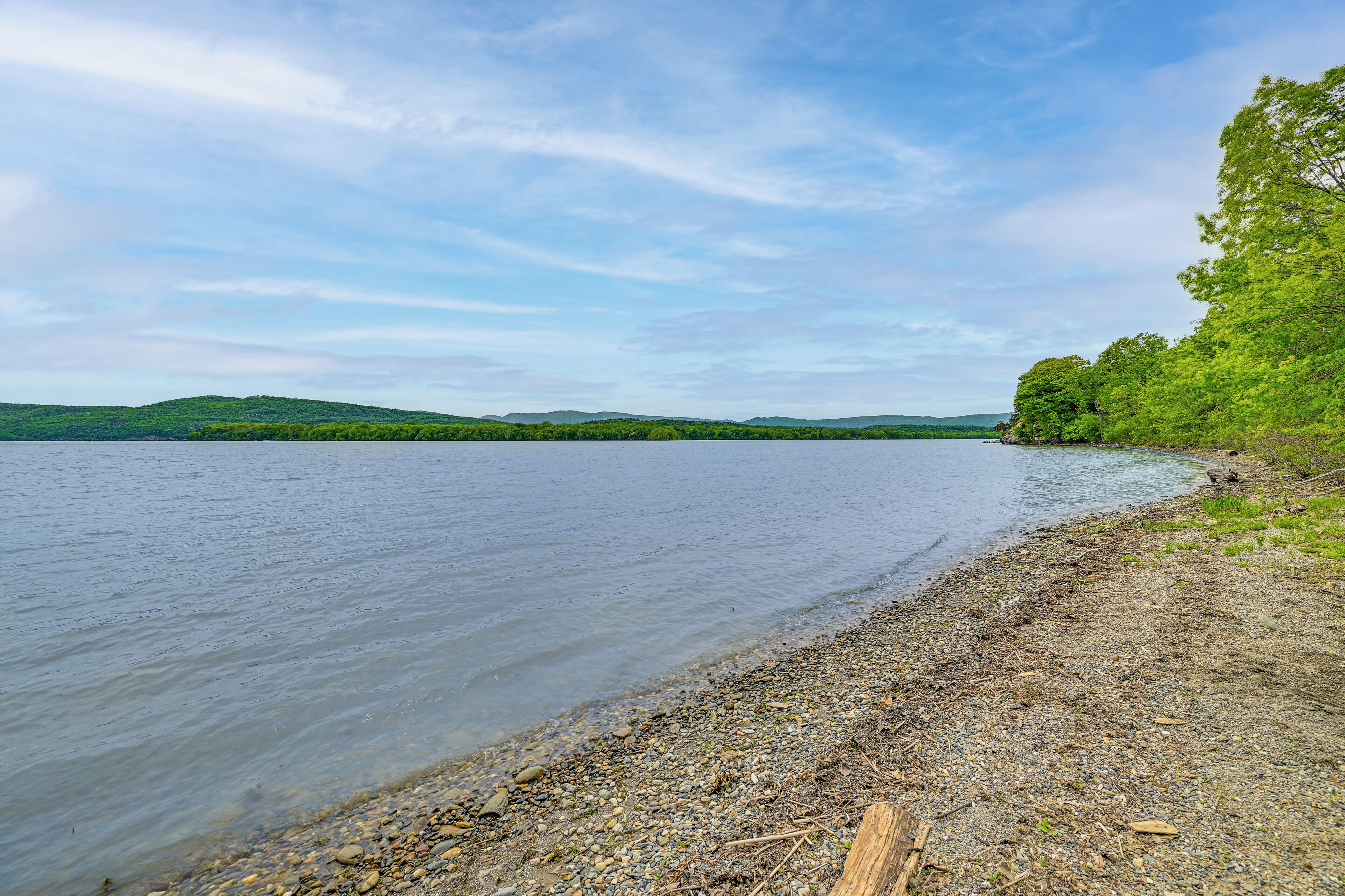 A calm lake with a pebbly shore and distant green hills.