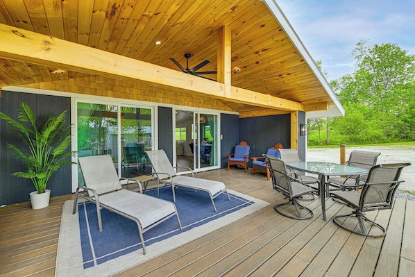 A covered outdoor area with a wooden deck, lounge chairs, a table, and chairs.