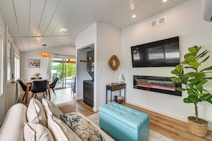 A modern living room with a sofa, a blue ottoman, a fireplace, and a dining area with a table and chairs.