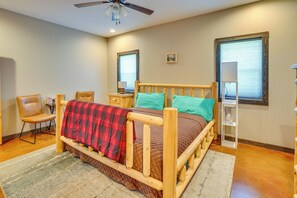 A bedroom with a wooden bed, a chair, a nightstand, a lamp, and a window.