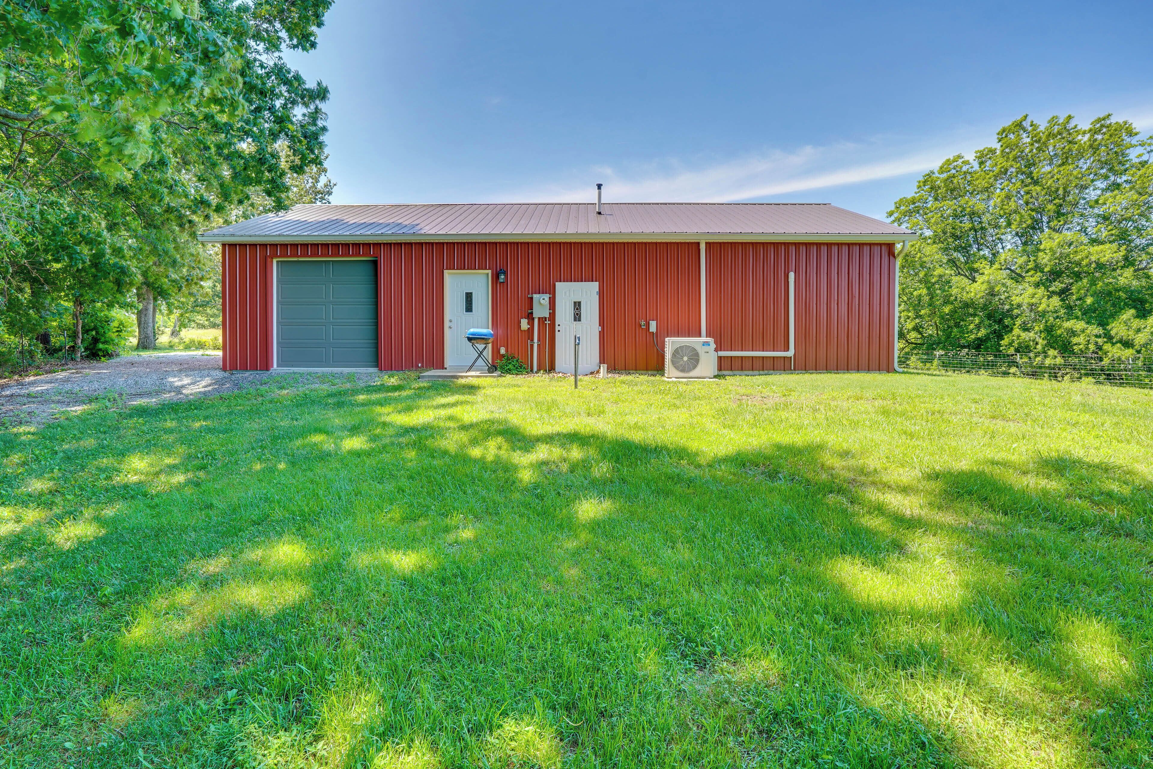 A red barn with a green garage door, a small chair, and an air conditioning unit.