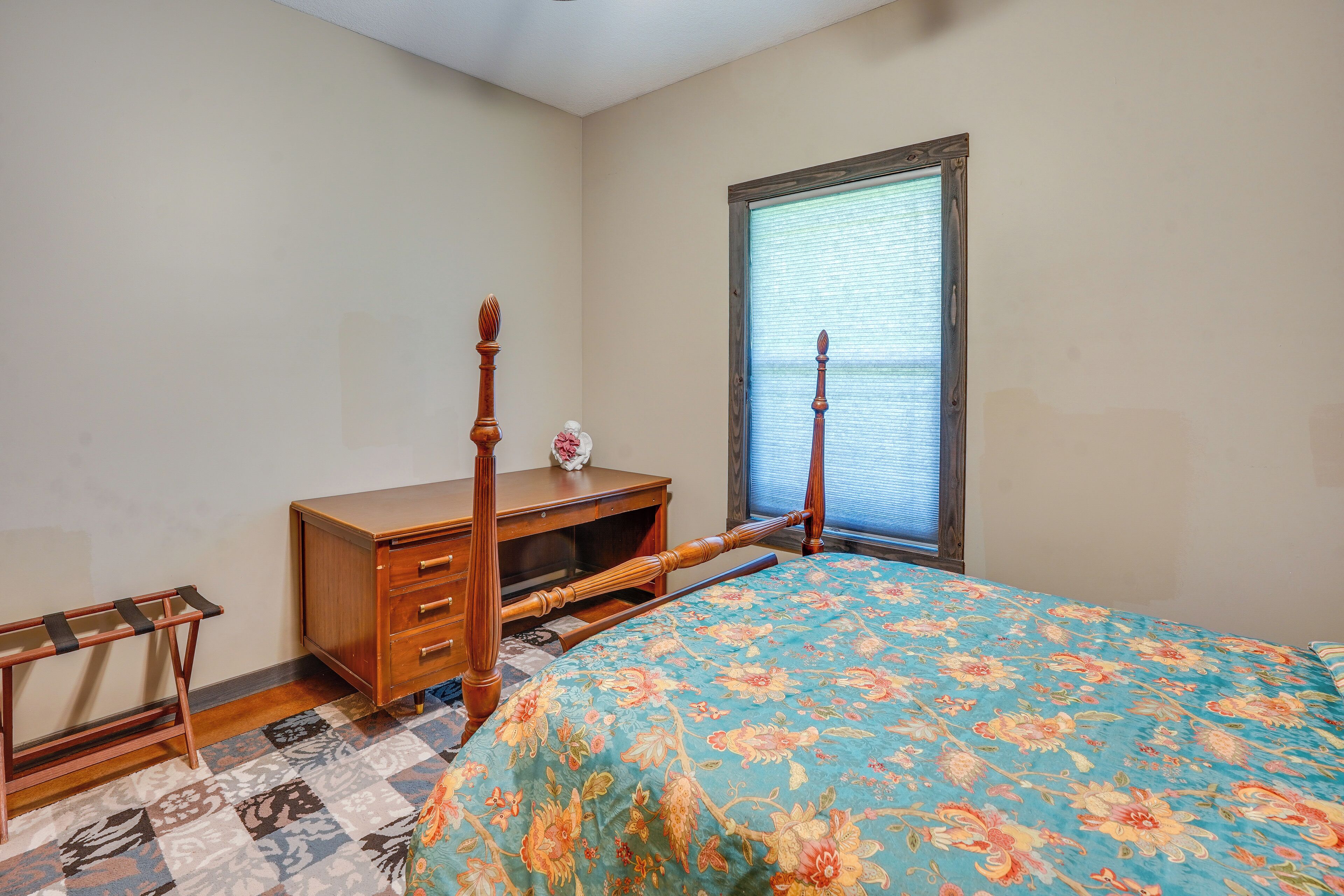A bedroom with a bed, wooden dresser, and a window with blinds.