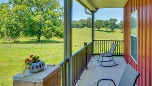 A porch with a view of a grassy field and trees, a rocking chair, and a potted plant. - Boaters Base! 11 Mi to Kentucky & Barkley Lakes (Grand Rivers)