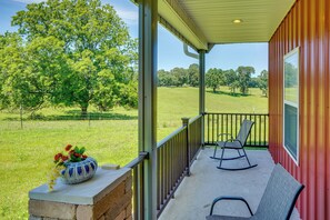 A porch with a view of a grassy field and trees, a rocking chair, and a potted plant. - Boaters Base! 11 Mi to Kentucky & Barkley Lakes (Grand Rivers)