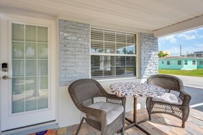 Eine überdachte Terrasse mit Korbstühlen, einem Tisch, einer Steinmauer und einer Tür mit Milchglas.
