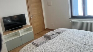 Un dormitorio con cama, televisor sobre un mueble, puerta de madera, aire acondicionado y ventana con persianas.
