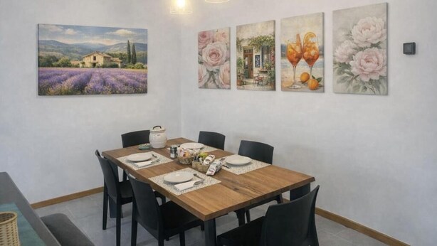 Un comedor con una mesa de madera, sillas negras y un cuadro de una casa en un campo.