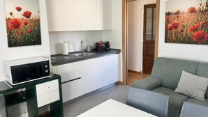 Una cocina moderna con armarios blancos, un microondas y una cafetera. En la zona de estar, hay un sofá verde y una mesa blanca.