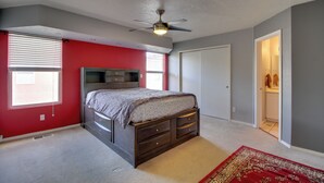 Um quarto com uma cama, um ventilador de teto, uma janela com persianas, uma porta e um tapete.